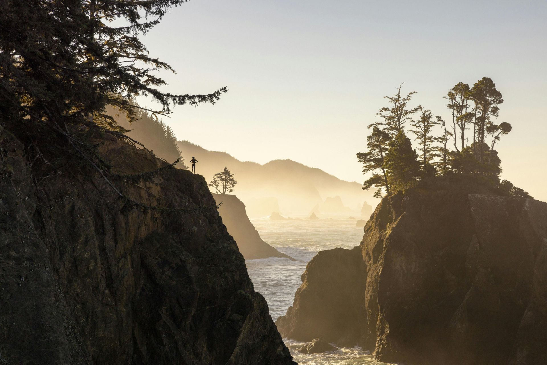 Majestic sunrise view of rugged coastal cliffs with a lone silhouette, creating a serene and dramatic seascape.
