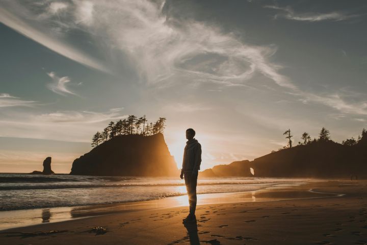 A lone figure stands silhouetted on a serene Washington beach at sunset, showcasing natural beauty and tranquility.
