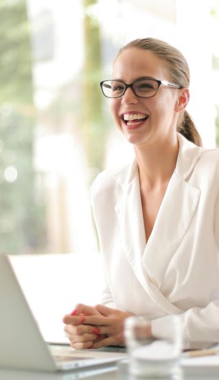 Cheerful businesswoman in glasses working on a laptop, in a bright and modern office setting.
