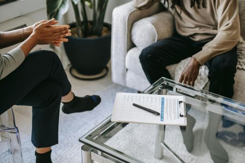 Crop anonymous African American man in casual clothes sitting on sofa and talking to female psychologist during psychotherapy session in modern studio