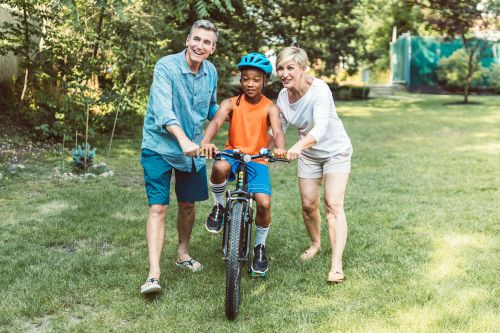 A family helps a young boy learn to ride a bicycle outdoors.