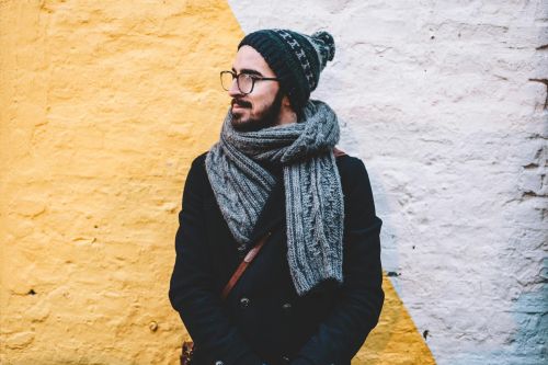 Man in winter attire with scarf and beanie looks away from camera against a vibrant wall.