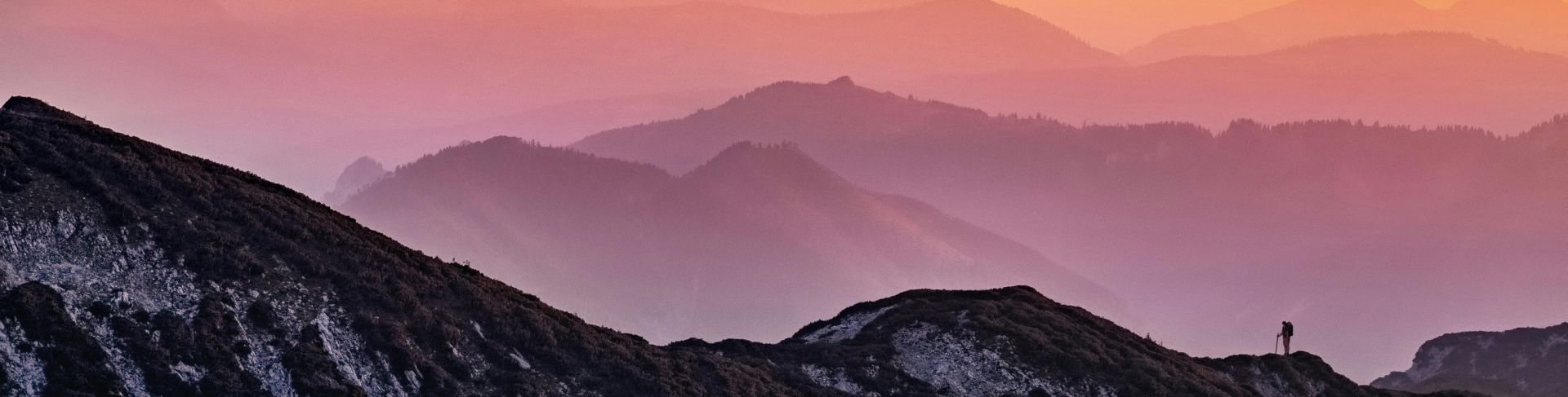 Colorful sunrise over misty mountains in Altmünster, Austria with a lone hiker silhouette.