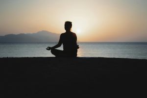 A woman practices meditation with a tranquil ocean sunset backdrop, embodying peace and relaxation.