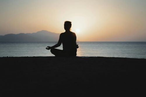 A woman practices meditation with a tranquil ocean sunset backdrop, embodying peace and relaxation.