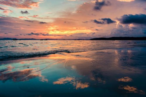 Stunning sunset over the ocean with vibrant reflections on a tranquil beach.