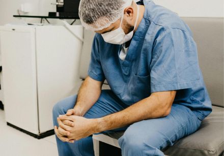 A male doctor in hospital attire sitting pensively, representing healthcare challenges.