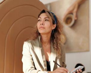 Confident woman in blazer taking notes with pen and smartphone in cafe.