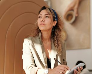 Confident woman in blazer taking notes with pen and smartphone in cafe.