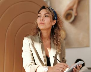 Confident woman in blazer taking notes with pen and smartphone in cafe.