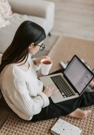 Adult woman in cozy sweater works on laptop while enjoying a hot drink indoors.