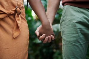 Close-up of an interracial couple holding hands in a natural outdoor setting, symbolizing love and unity.
