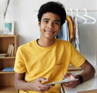 Happy teenage boy sitting indoors using a tablet for online learning.
