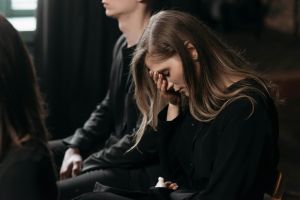 A woman in black clothing expresses sorrow at a funeral, reflecting on loss.