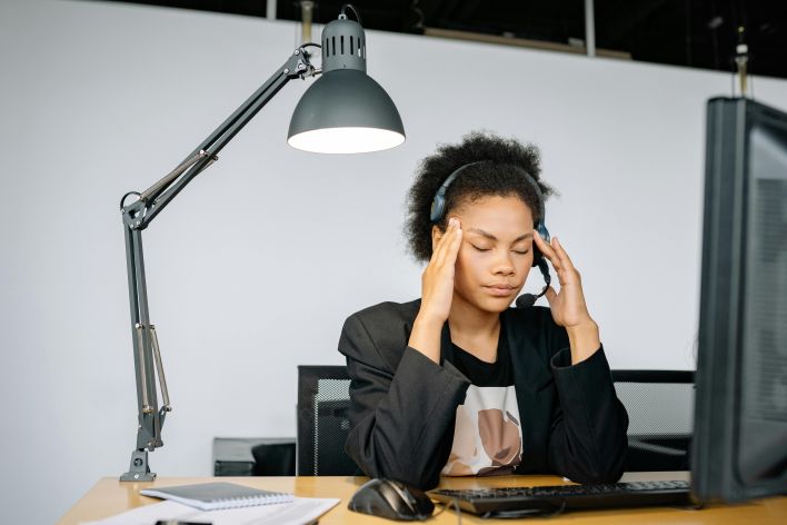 Exhausted call center agent with headset, tired from work, in an indoor office setting.