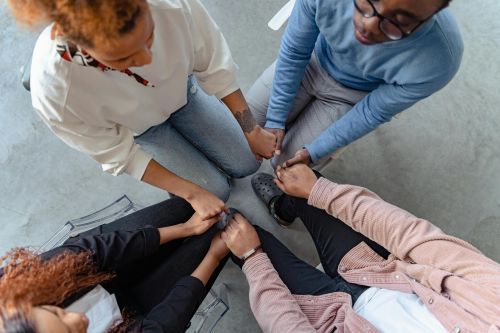 Four people sit in a circle holding hands, emphasizing unity and support in a therapy session.