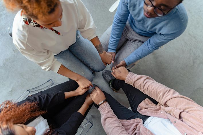 Four people sit in a circle holding hands, emphasizing unity and support in a therapy session.