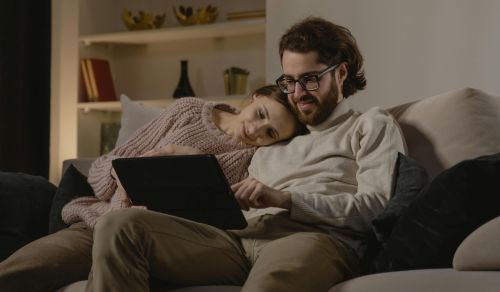 A couple sharing a relaxed moment on a cozy couch, browsing a tablet.