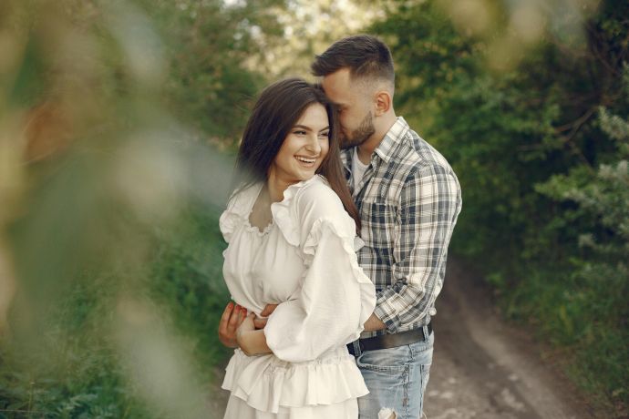 A joyful couple embracing outdoors on a sunny day, surrounded by lush greenery.