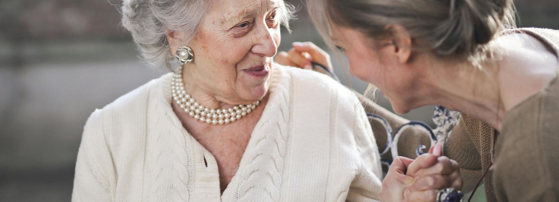 Joyful interaction between an elderly woman and her granddaughter in a sunny outdoor setting.