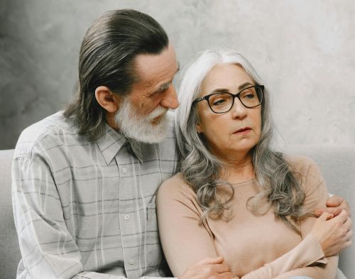 Elderly couple sitting closely, expressing comfort and support in a cozy living room setting.