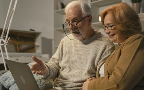 Senior couple smiling and gesturing during a video call on a laptop at home.