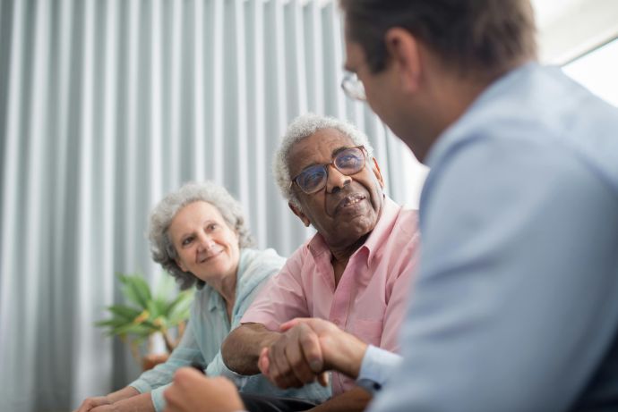 Elderly couple discussing with a consultant indoors, expressing interest and connection.